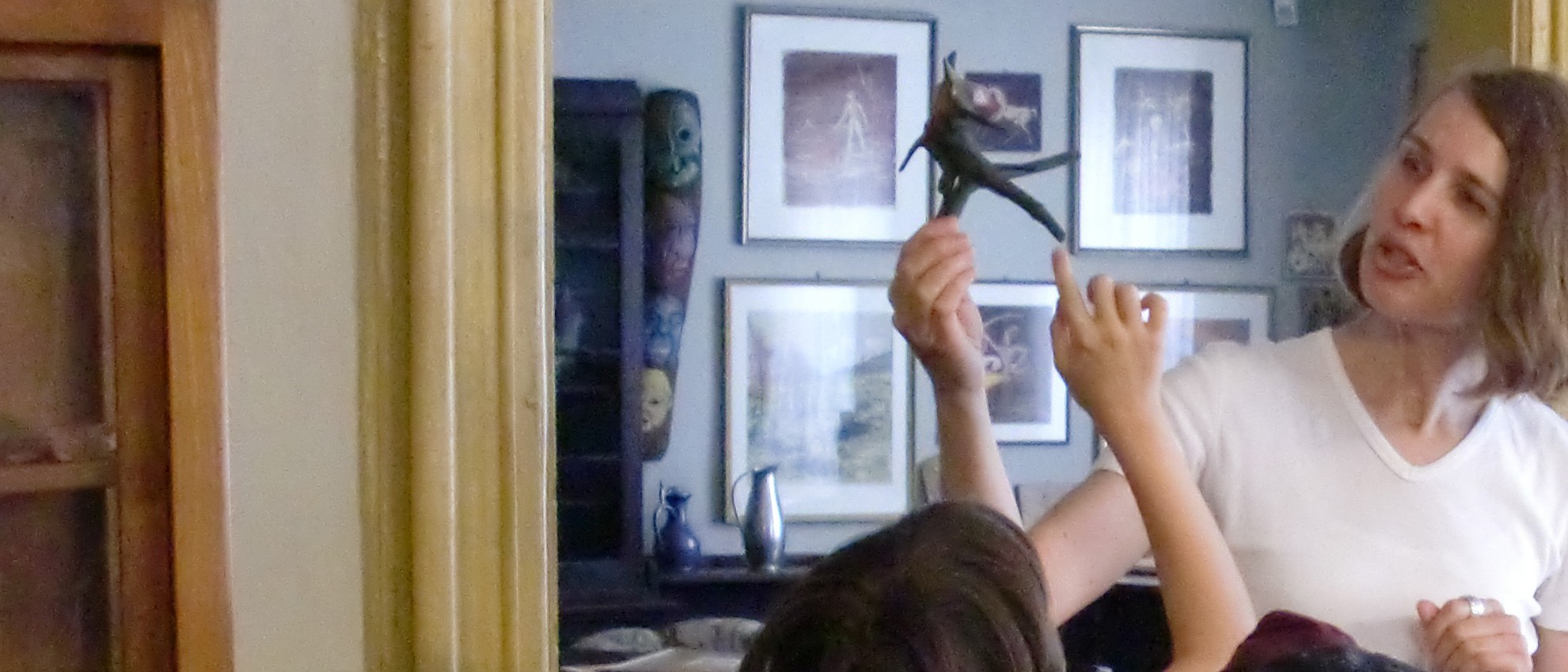 Das Foto zeigt Christa Haubelt-Schlosser mit einer Gruppe von Kindern im Museum des Schmidt-Hauses. Sie hält eine Wurzelplastik von Karl Schmidt in der Hand. Im Hintergrund der Blick in das Wohnzimmer des Künstlers.