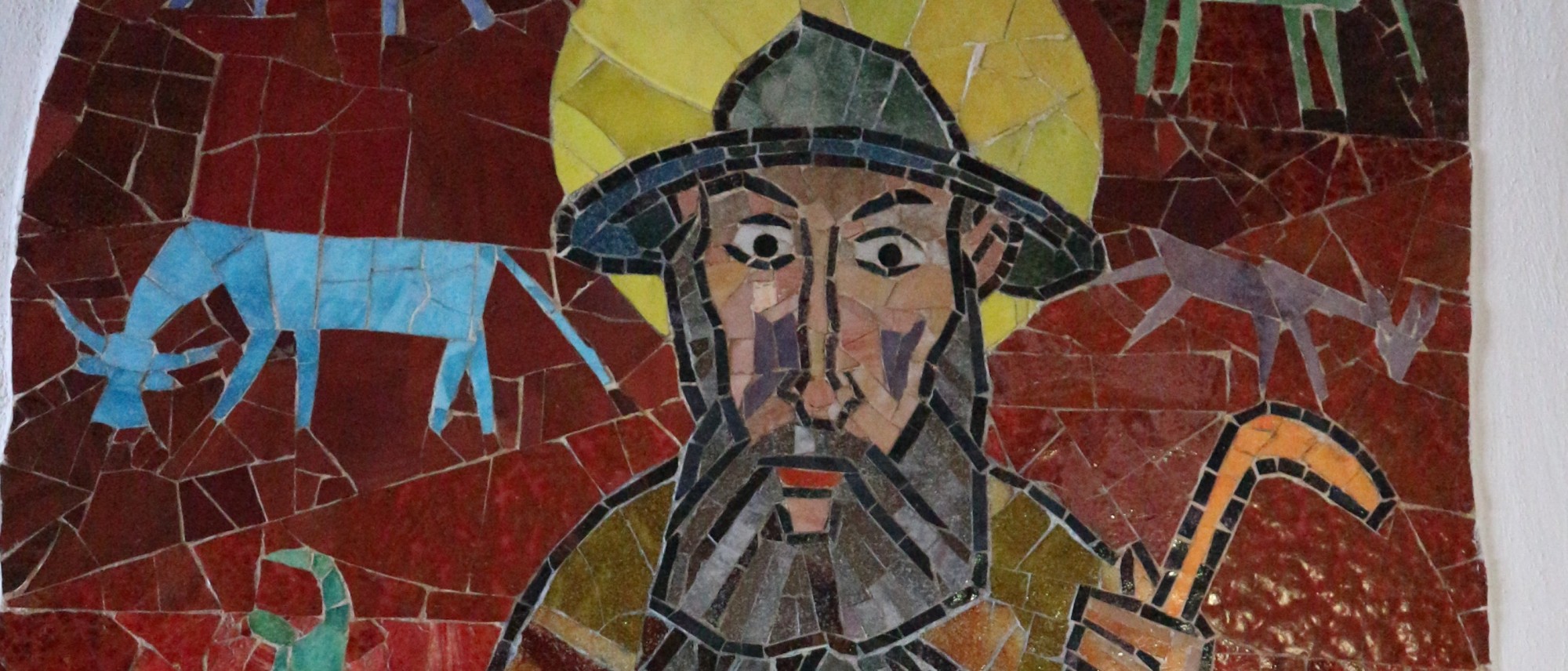 Das Foto zeigt einen Teil eines bunten Mosaiks. Es ist der hl. Leonhard als Benediktiner sowie links neben ihm eine Kuh und rechts eine Ziege zu sehen.