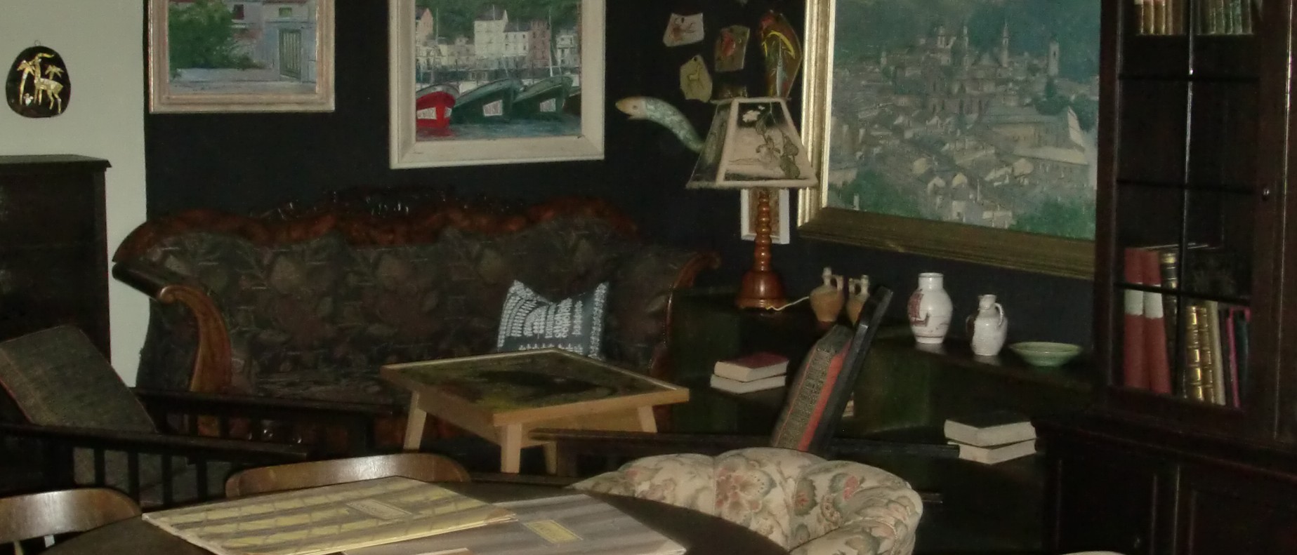 Das Foto zeigt einen Ausschnitt des Wohnzimmers von Karl Schmidt. Man sieht Bilder und andere Kunstobjekte an den Wänden sowie ein Sofa, Regale, Stühle und einen Mosaiktisch.