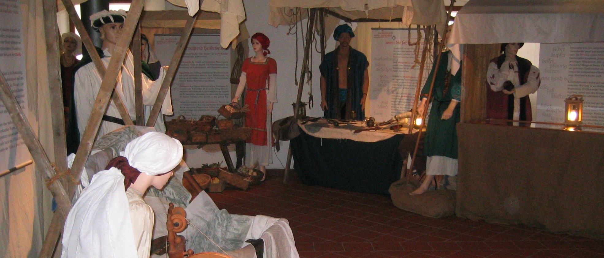 Das Foto zeigt einen Ausschnitt der Ausstellung &quot;Des Marktes wahre Geschichten&quot;. Man sieht Marktstände, dazwischen menschengroße Puppen in mittelalterlicher Gewandung, die unterschiedliche Waren anbieten.
